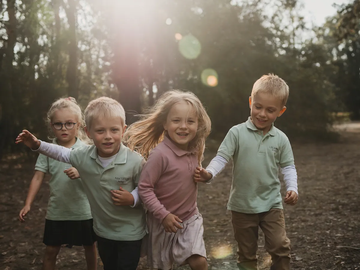 Four children walking arm in arm through sunlit woods