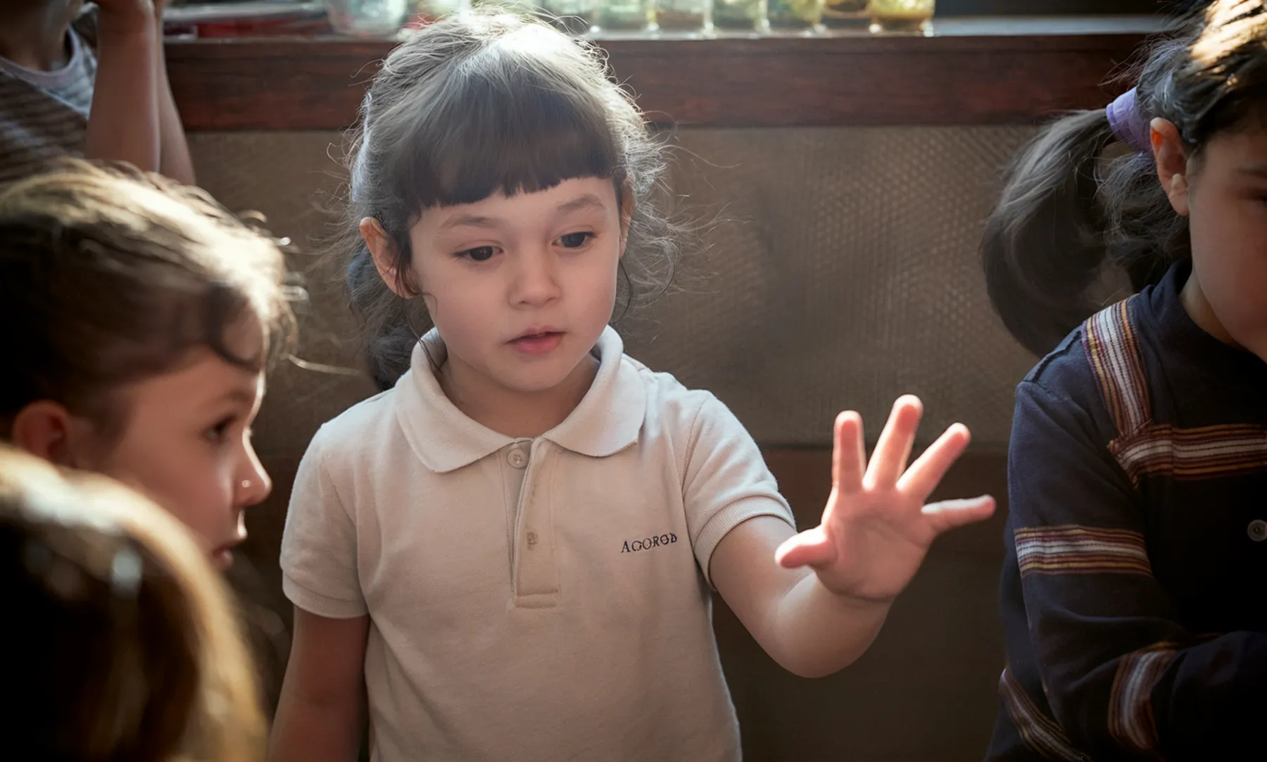 Children in a warm-lit classroom raising their hands together in the 5-day academy
